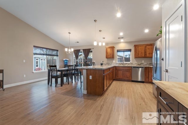 kitchen featuring brown cabinets, light wood-style flooring, a kitchen breakfast bar, stainless steel appliances, and a peninsula