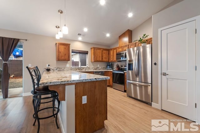 kitchen featuring a breakfast bar area, light wood-type flooring, brown cabinets, appliances with stainless steel finishes, and a peninsula