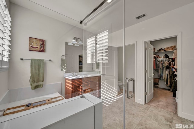 bathroom with toilet, vanity, visible vents, and a walk in closet