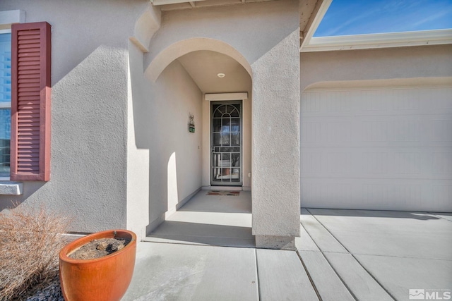 entrance to property with a garage and stucco siding