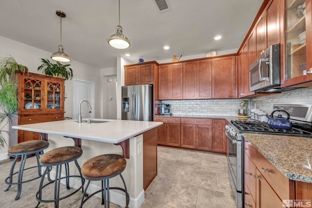 kitchen featuring stainless steel appliances, visible vents, backsplash, a kitchen island with sink, and a sink