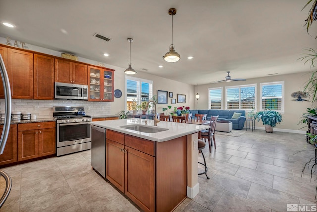 kitchen featuring stainless steel appliances, tasteful backsplash, visible vents, brown cabinetry, and a sink