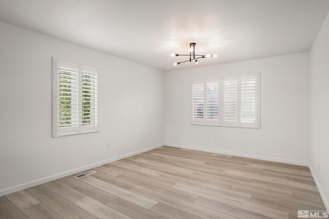 spare room with a chandelier, light wood-type flooring, visible vents, and baseboards