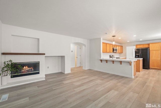 unfurnished living room featuring light wood finished floors, visible vents, arched walkways, a tile fireplace, and recessed lighting