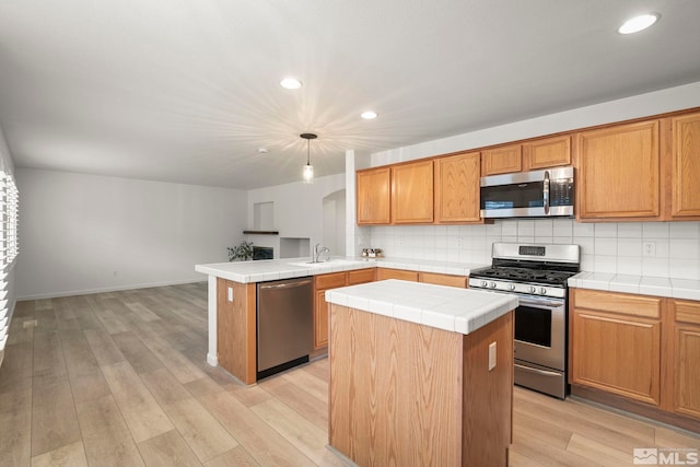 kitchen with stainless steel appliances, tile counters, light wood-type flooring, and tasteful backsplash