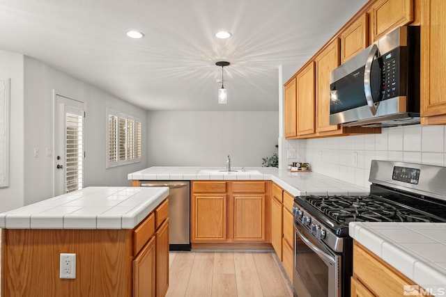 kitchen featuring tile countertops, backsplash, appliances with stainless steel finishes, light wood-style floors, and a peninsula