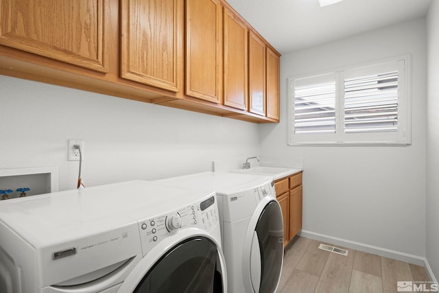 washroom featuring light wood finished floors, cabinet space, visible vents, a sink, and separate washer and dryer