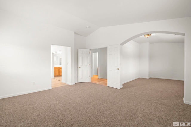 unfurnished room with arched walkways, light carpet, vaulted ceiling, and baseboards