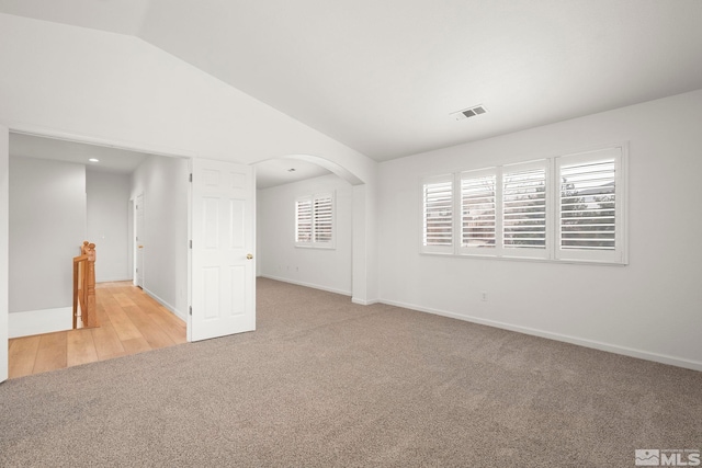 spare room featuring visible vents, arched walkways, baseboards, light colored carpet, and lofted ceiling