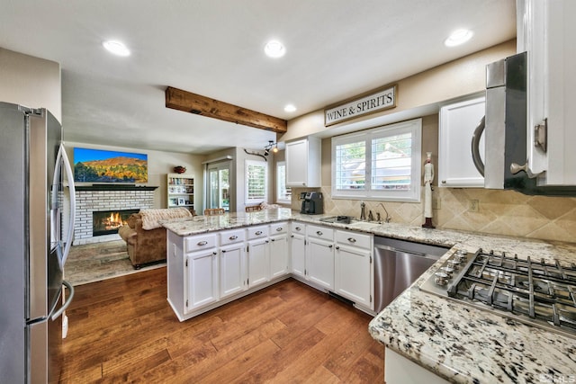 kitchen with dark wood-type flooring, a peninsula, stainless steel appliances, a fireplace, and a sink