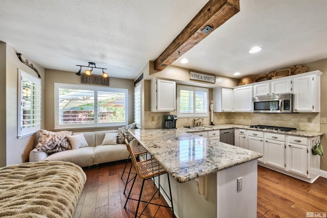 kitchen with a breakfast bar, stainless steel appliances, tasteful backsplash, a peninsula, and hardwood / wood-style floors