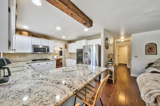 kitchen featuring light stone counters, appliances with stainless steel finishes, dark wood-type flooring, a peninsula, and a kitchen bar