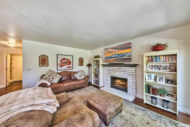 living room featuring a brick fireplace, a textured ceiling, baseboards, and wood finished floors