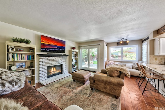 living room featuring a textured ceiling, a brick fireplace, and wood finished floors