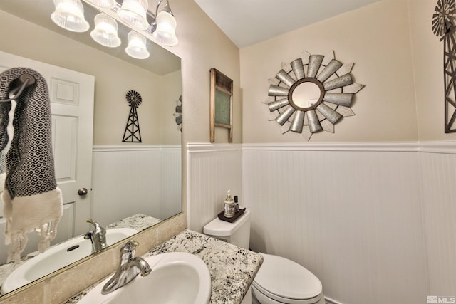 bathroom with wainscoting, vanity, toilet, and an inviting chandelier