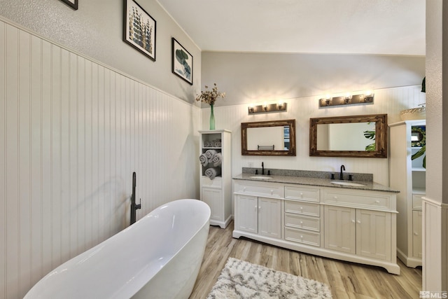 bathroom featuring double vanity, a sink, a freestanding bath, and wood finished floors