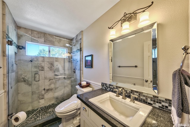 bathroom with backsplash, toilet, a stall shower, vanity, and a textured ceiling