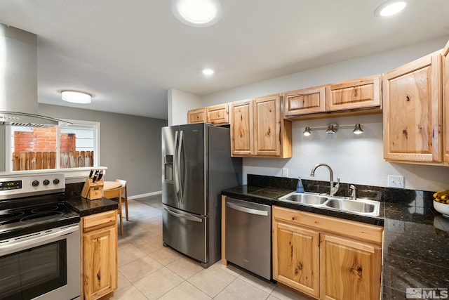 kitchen featuring tile countertops, stainless steel appliances, light brown cabinetry, wall chimney range hood, and a sink