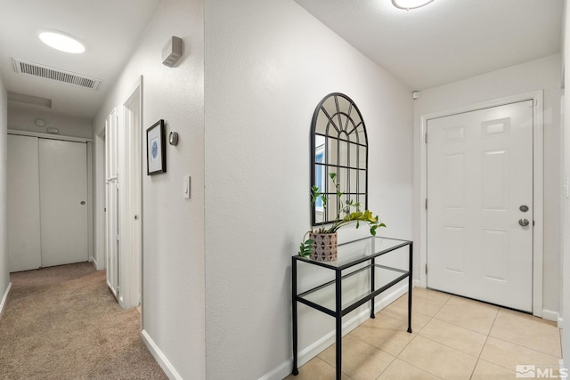 foyer entrance featuring light colored carpet, visible vents, baseboards, and light tile patterned flooring