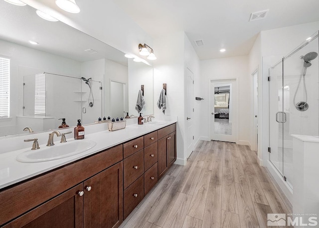 bathroom with wood finished floors, a stall shower, a sink, and visible vents