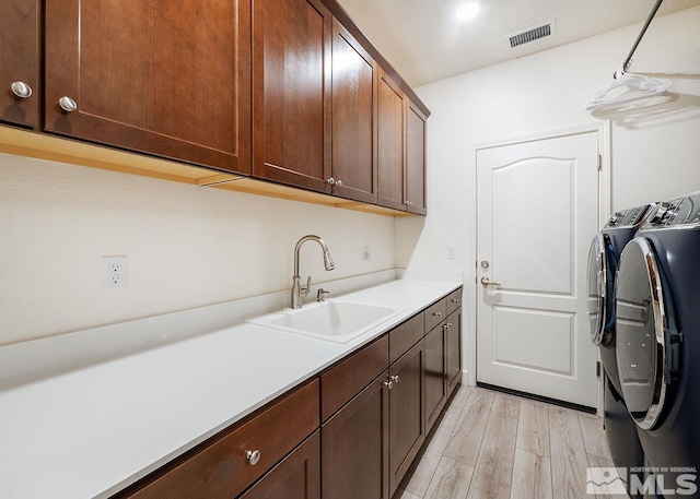 laundry area with a sink, visible vents, light wood-style floors, cabinet space, and washer and clothes dryer