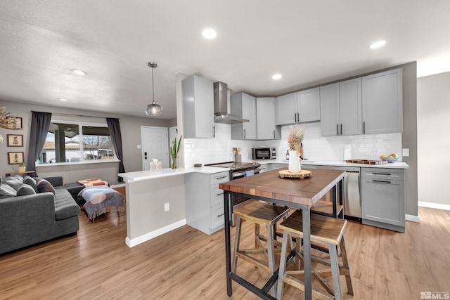 kitchen featuring wall chimney exhaust hood, light wood finished floors, light countertops, and stainless steel appliances