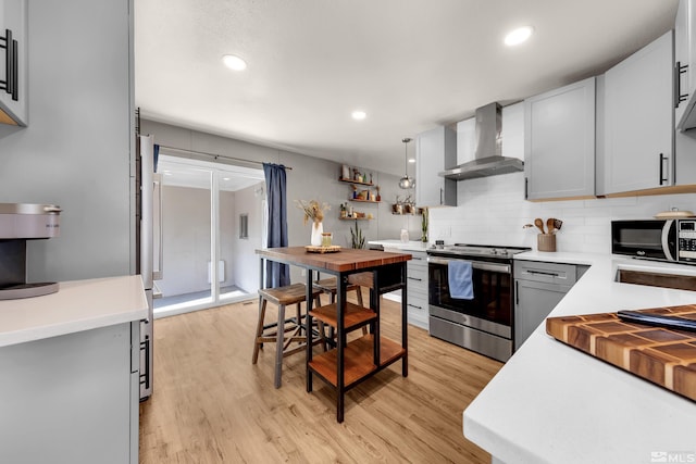 kitchen with stainless steel electric range oven, light countertops, light wood-style flooring, decorative backsplash, and wall chimney exhaust hood