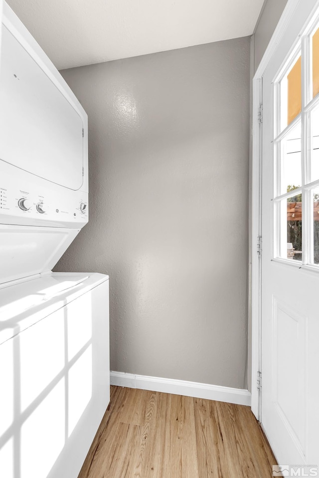 washroom featuring laundry area, light wood finished floors, stacked washing maching and dryer, and baseboards