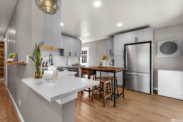 kitchen featuring stainless steel appliances, a sink, light wood-style flooring, and decorative backsplash