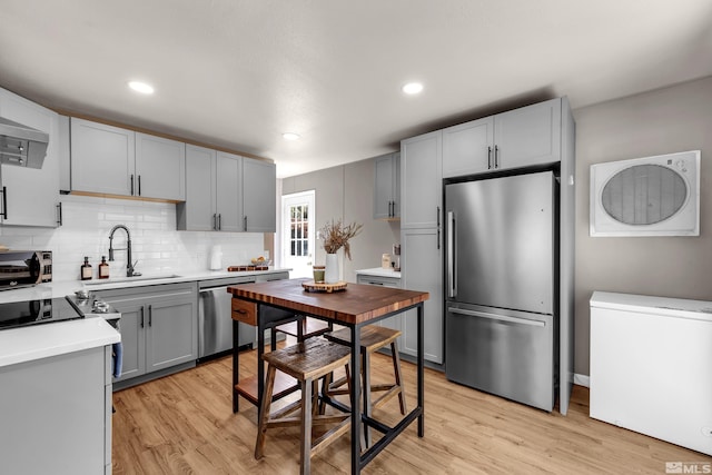 kitchen with light countertops, backsplash, appliances with stainless steel finishes, light wood-style floors, and a sink