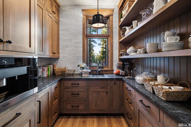 kitchen with open shelves, backsplash, light wood-style flooring, a sink, and dark stone counters