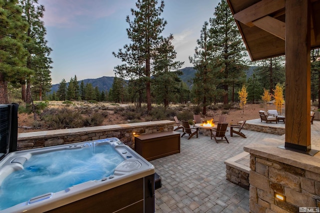 view of patio featuring a hot tub, a fire pit, and a mountain view