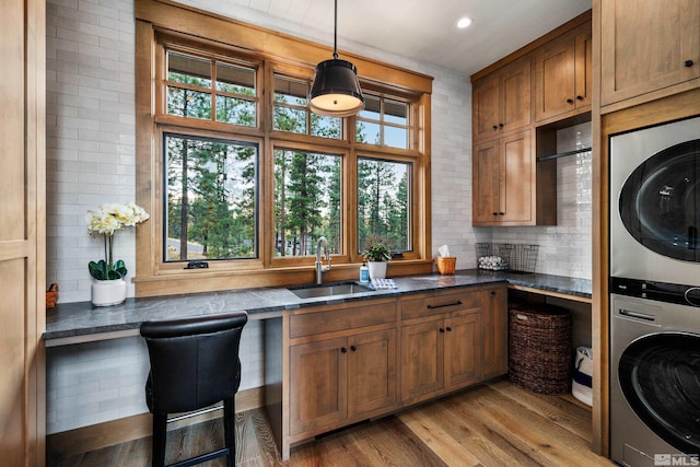 kitchen featuring a sink, stacked washer / drying machine, light wood-type flooring, dark countertops, and decorative light fixtures