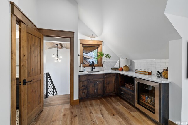 bar with lofted ceiling, beverage cooler, a sink, and light wood-style flooring