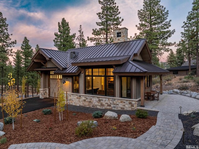 view of front facade featuring stone siding, a chimney, metal roof, an attached garage, and a standing seam roof