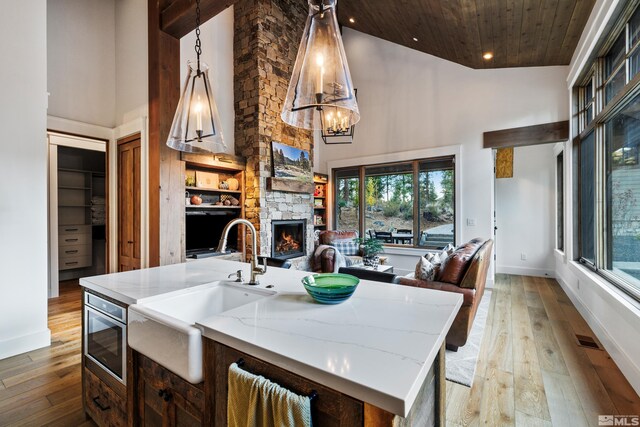 kitchen with a fireplace, stainless steel microwave, light wood-style floors, open floor plan, and high vaulted ceiling