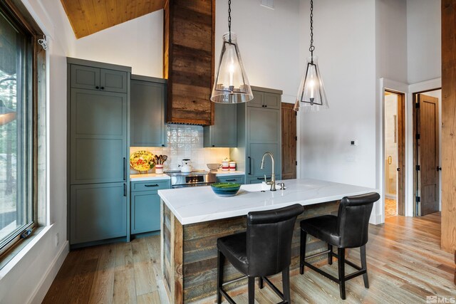 kitchen featuring decorative light fixtures, a breakfast bar area, tasteful backsplash, light wood-style flooring, and high vaulted ceiling