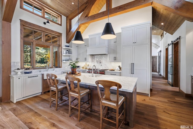 kitchen with backsplash, a barn door, a kitchen island with sink, high vaulted ceiling, and wooden ceiling