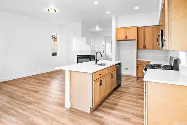 kitchen with a kitchen island with sink, light wood-style flooring, a sink, open floor plan, and appliances with stainless steel finishes