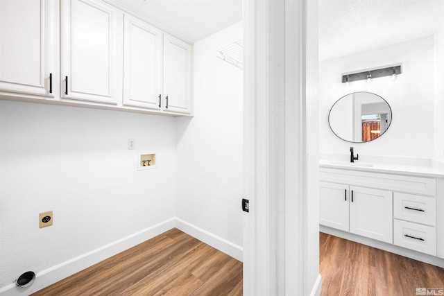 clothes washing area with light wood finished floors, cabinet space, hookup for an electric dryer, a sink, and baseboards