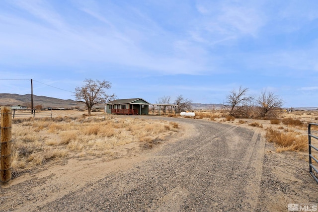 view of street with dirt driveway, a rural view, a mountain view, and a gated entry