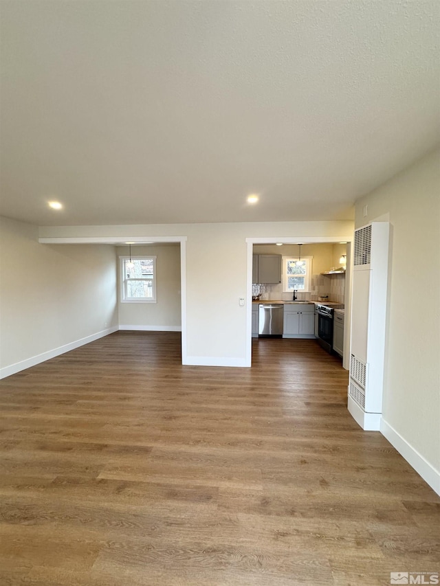 unfurnished living room with recessed lighting, a sink, baseboards, and wood finished floors