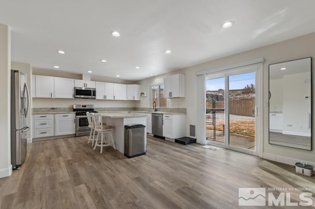 kitchen with stainless steel appliances, wood finished floors, white cabinetry, a center island, and a kitchen bar