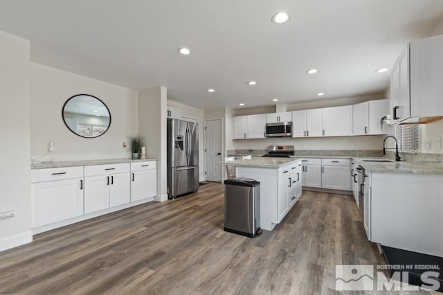 kitchen featuring dark wood-style flooring, a center island, stainless steel appliances, white cabinetry, and a sink