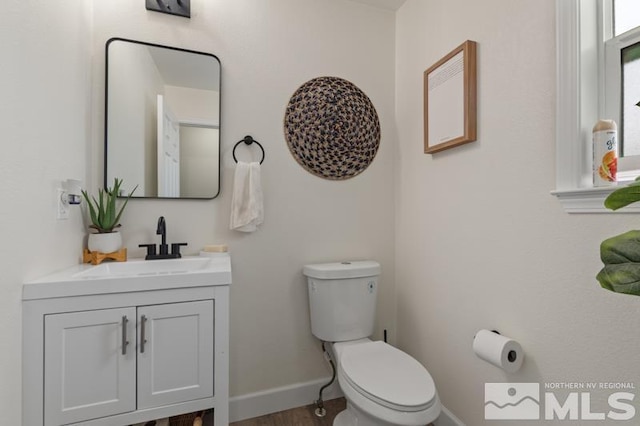 half bathroom with toilet, baseboards, and vanity