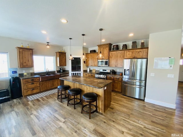 kitchen with a center island, a breakfast bar, dark countertops, appliances with stainless steel finishes, and brown cabinetry