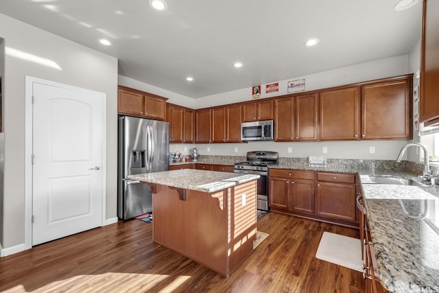 kitchen featuring brown cabinets, dark wood-type flooring, a sink, light stone counters, and stainless steel appliances