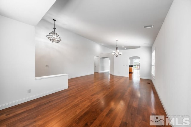 unfurnished living room featuring arched walkways, a chandelier, wood finished floors, baseboards, and vaulted ceiling