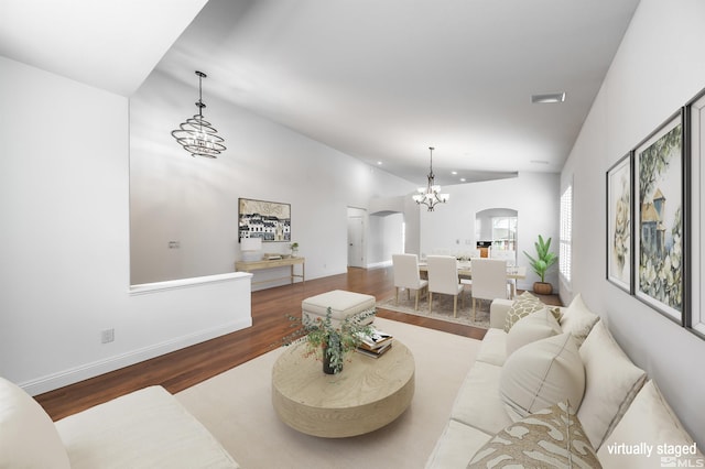 living room featuring arched walkways, wood finished floors, baseboards, vaulted ceiling, and an inviting chandelier