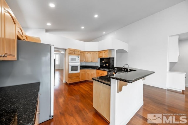 kitchen with dark wood finished floors, appliances with stainless steel finishes, a sink, a peninsula, and a kitchen bar